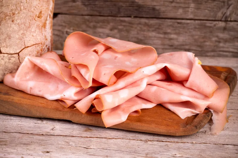 slices of fresh mortadella and bread on wooden board