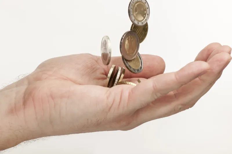 side detail view in a male hand of falling euro coins against a white background, self portrait, own hand