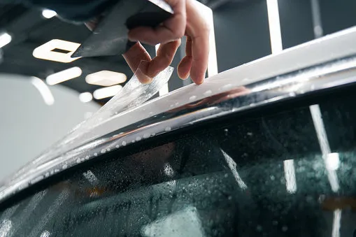 cropped photo of worker installing clear paint protection film on car roof