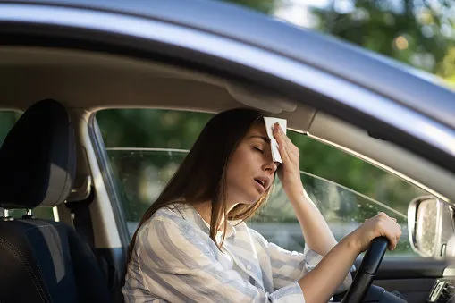 girl driver being hot during heat wave in car, suffering from hot weather, has problem with a non-working air conditioner, wipes sweat from her forehead with tissue summer, heat concept