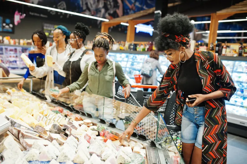 group of five african womans with shopping carts choose cheese in supermarket