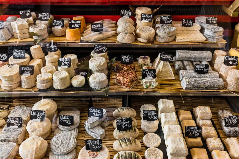 a large selection of different french and italian cheeses on the counter of a small store at the aligre market (marche d'aligre) in the bastille district paris, france