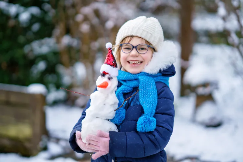 cute little preschool girl with glasses making mini snowman adorable healthy happy child playing and having fun with snow, outdoors on cold day active leisure with children in winter