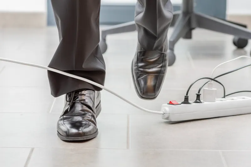 close up of a businessman legs stumbling with an electrical cord at office