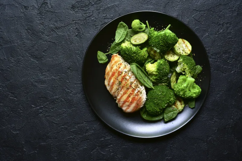 grilled chicken fillet with green vegetable salad on a black slate, stone or concrete backgroundtop view with copy space