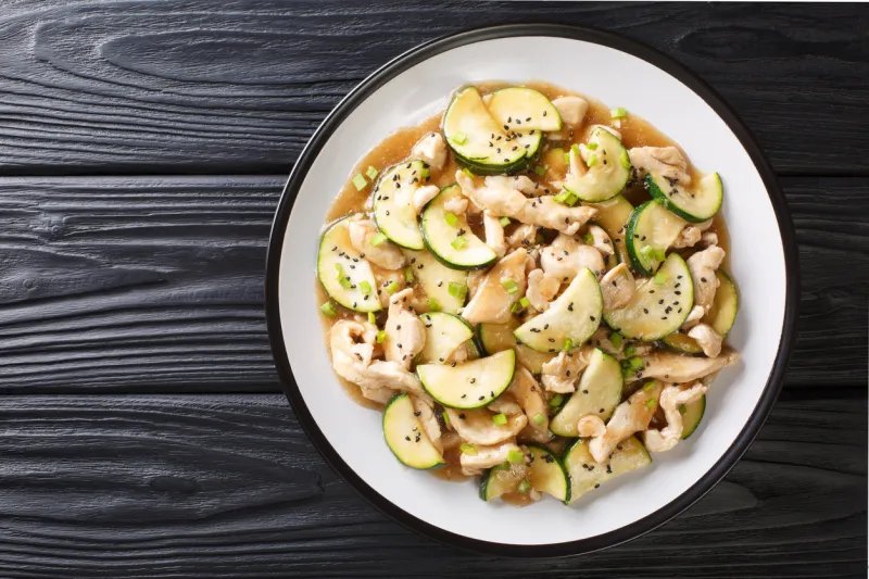 chinese cuisine fried chicken fillet with zucchini, sesame seeds and onions close-up on a plate on the table horizontal top view from above