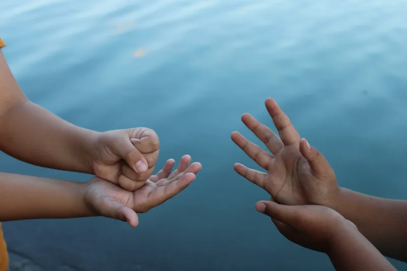 children playing rock paper scissors by the lake