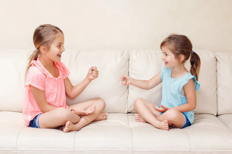 two girls friends playing rock paper scissors hand game caucasian children sitting on a couch playing together interesting entertaining activity for kids authentic candid lifestyle moment