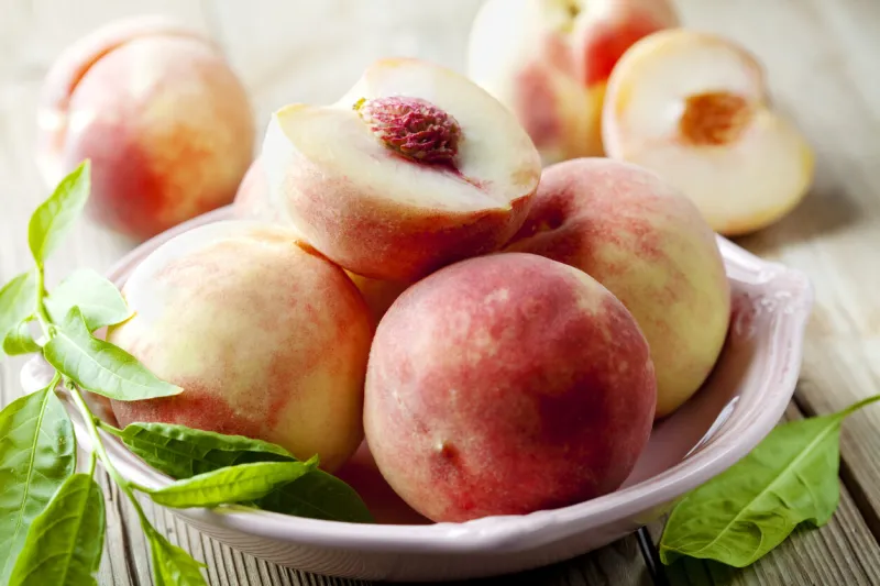 white peaches in a bowl with green leaves
