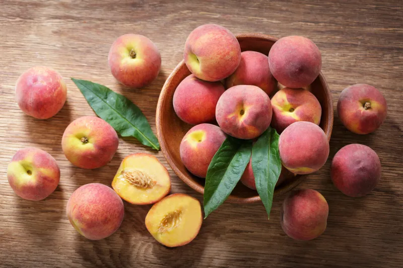 fresh ripe peaches in a bowl on a wooden table, top view