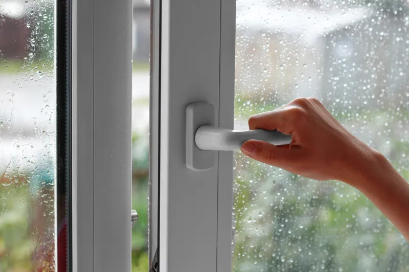 a female hand opens a window with water drops closes the window in the rainy weather closeup