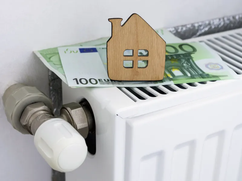 a small wooden house on the background of euro banknotes and radiator heating payment for heating in winter symbolic image, selective focus
