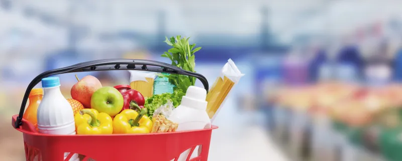 shopping basket filled with goods, supermarket aisle in the background, grocery shopping concept