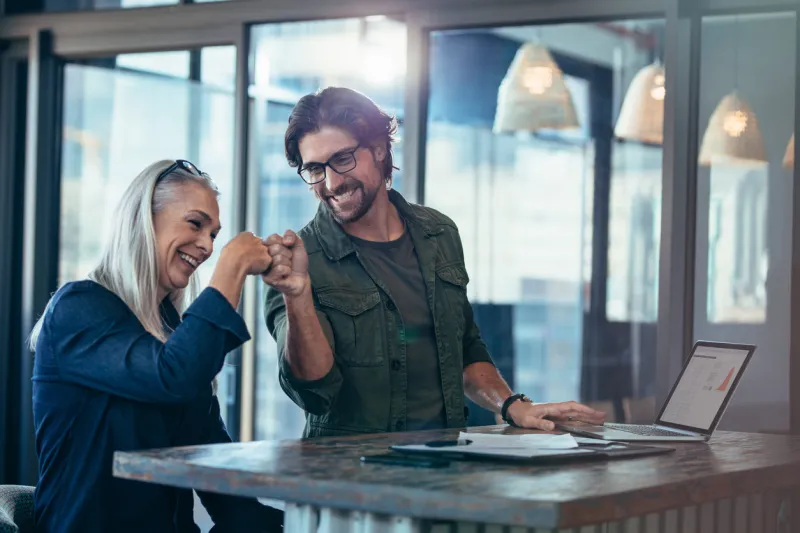 young businessman and senior businesswoman making a fist bump at office business colleagues looking happy and excited after completion of project