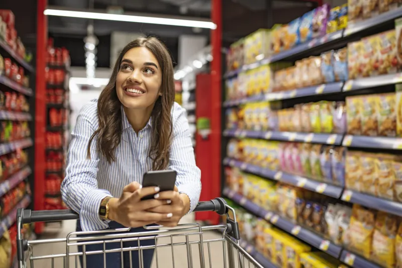smiling woman at supermarket happy woman at supermarket beautiful young woman shopping in a grocery store supermarket shopping lists in app format