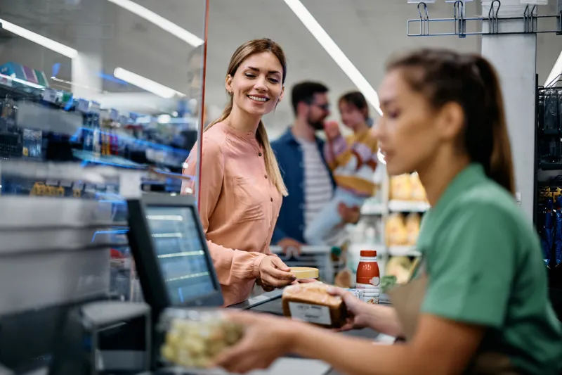 happy woman paying for groceries at checkout while buying with her family in supermarket