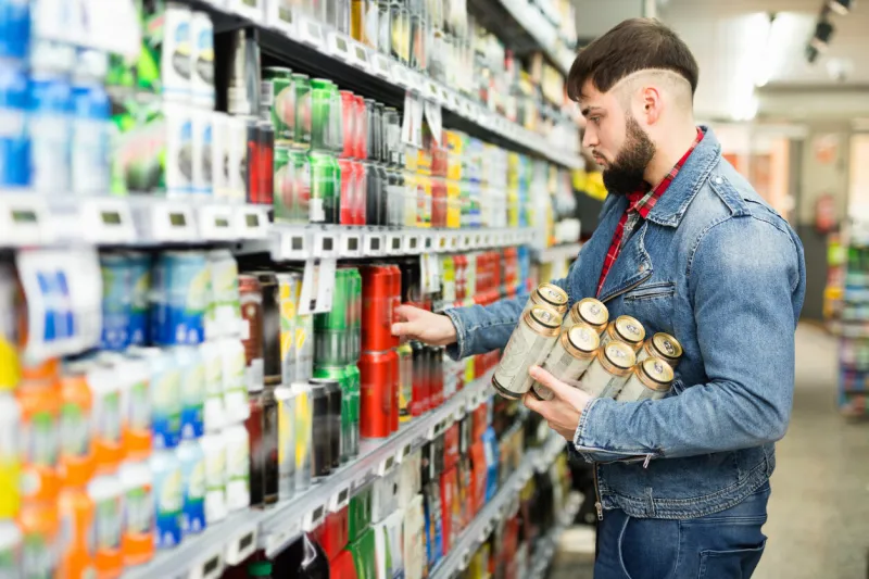 interested young cheerful positive man making purchases in grocery store, buying canned beer