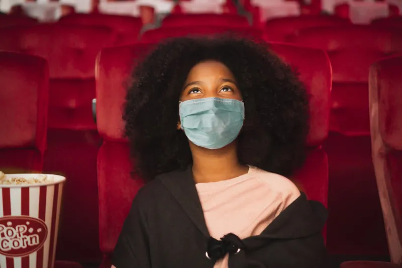 happy african kid wearing protective face mask and watching movie in theater theatre cinema protect infection from coronavirus covid-19, social distancing in theatre concept
