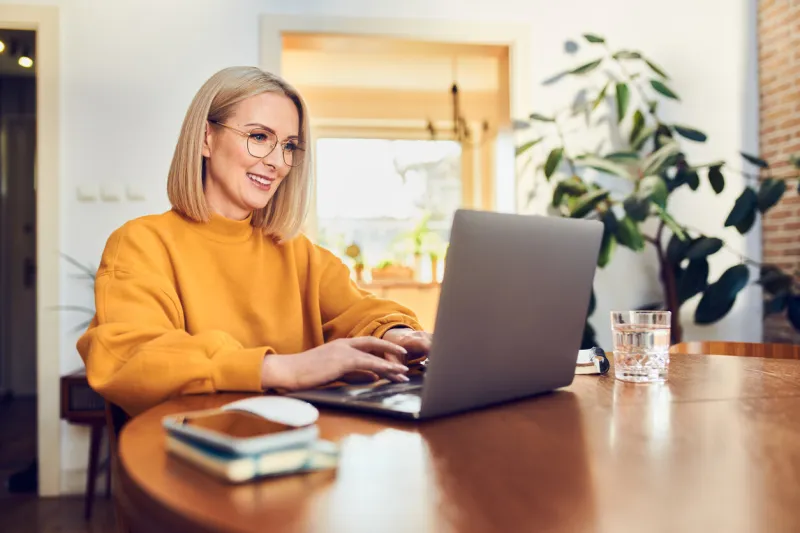 portrait of middle aged woman sitting at dinning with laptop working at home