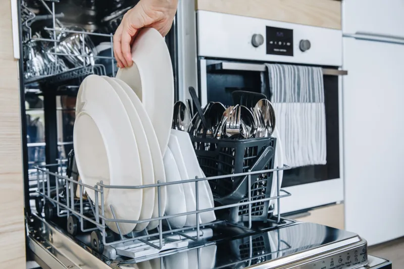 woman loading the dishwasher open dishwasher with clean glasses and dishes close-up after washing clean in open dishwashing machine