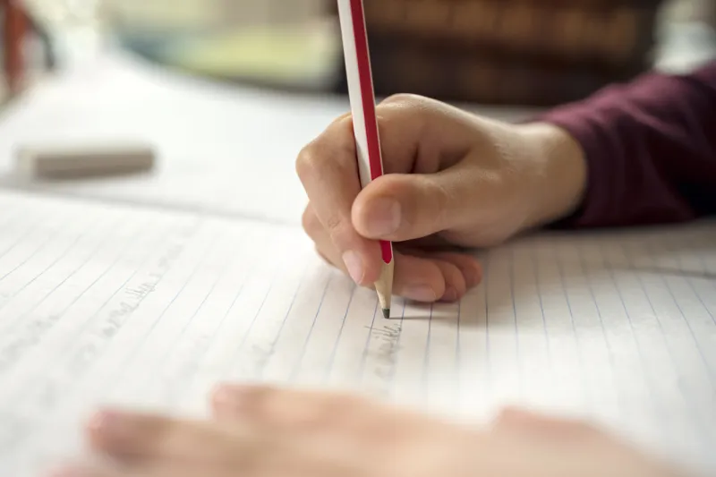boy writing in a notepad doing his school work spelling or homework