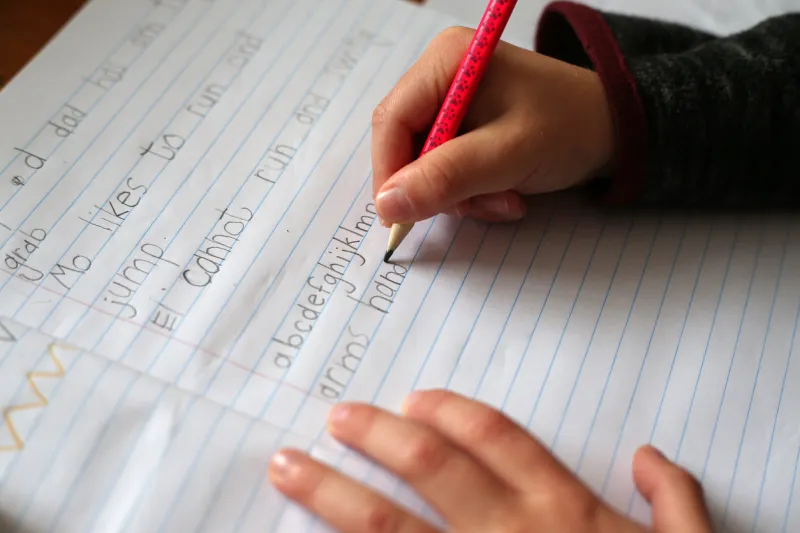 a young boy practices writing alphabet characters while homeschooling