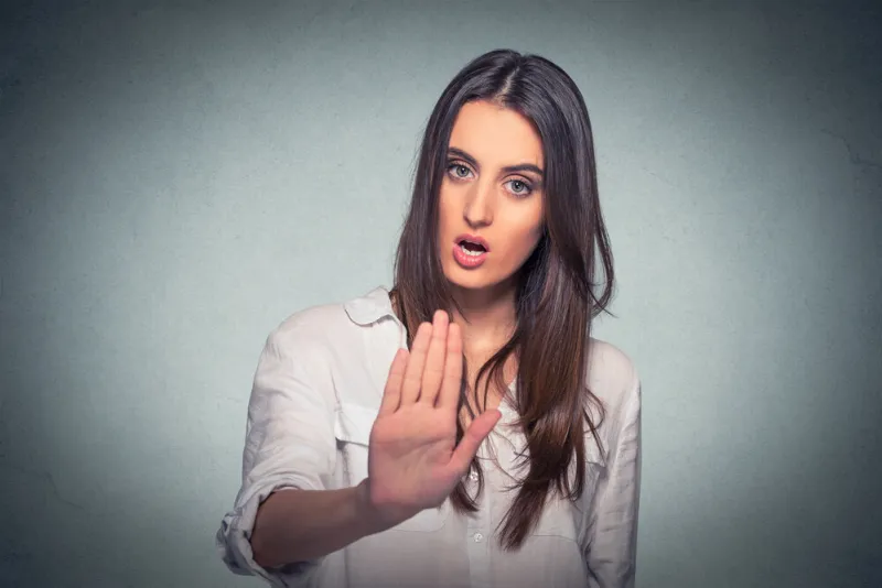young annoyed angry woman with bad attitude giving talk to hand gesture with palm outward isolated grey wall background negative human emotion face expression feeling body language