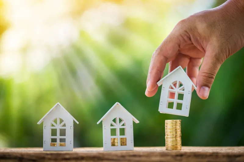 man hand hold a wooden home model put on the stack coin with growing in the public park, savings money for buy house and loan to business investment for real estate concept