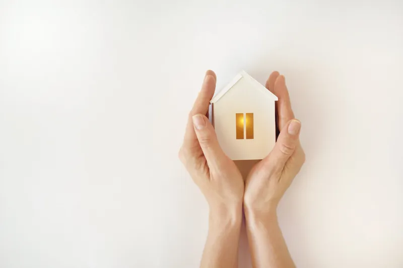 the model of the white house with warm light inside in female hands on a white background