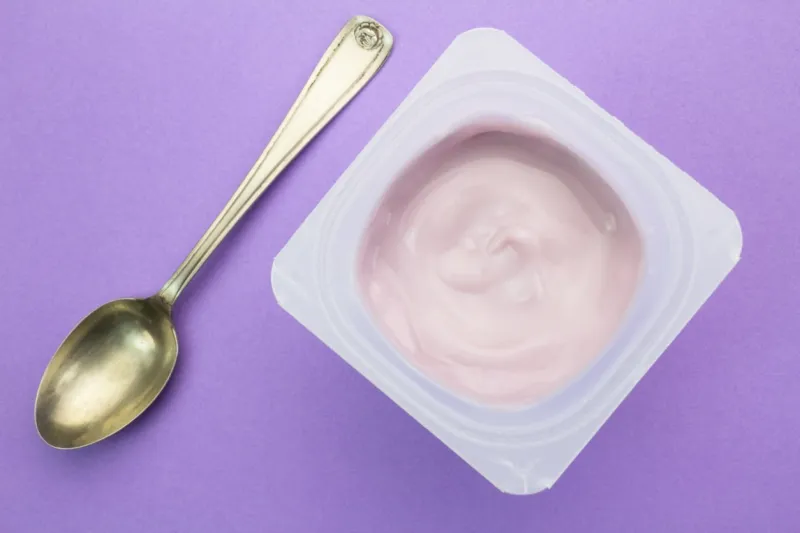 healthy strawberry fruit flavored yoghurt with natural coloring in plastic cup isolated on purple background with small silver spoon - top view
