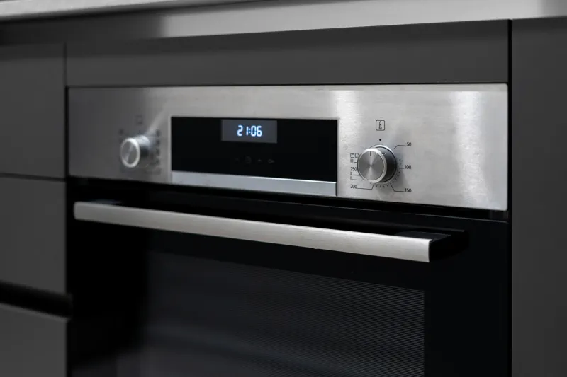 selective focus on built in oven appliance with time settings on display and buttons at control panel modern kitchen in contemporary apartment