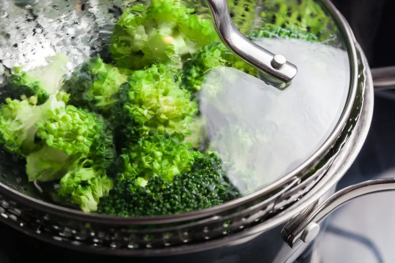 freshly steamed green broccoli in skimmer pot preparing vegetables concept