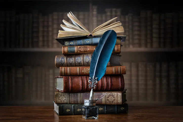 old books ,quill pen and vintage inkwell on wooden desk in old library ancient books historical background retro style conceptual background on history, education, literature topics