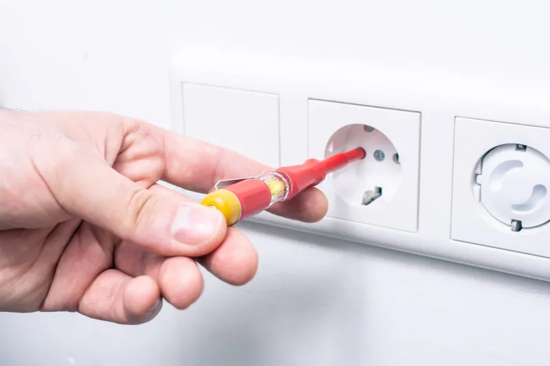 the hand of an electrician holding a phase tester in a wall socket, the glowing light indicates an active current