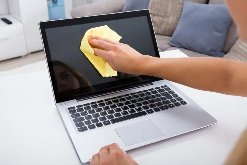 close-up of woman hand cleaning laptop screen with laptop at home