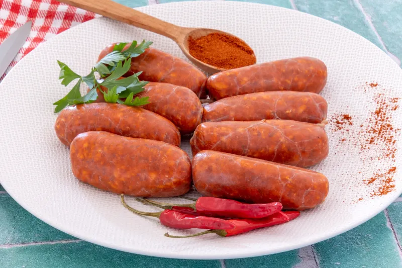 raw chorizos on a white plate with small peppers