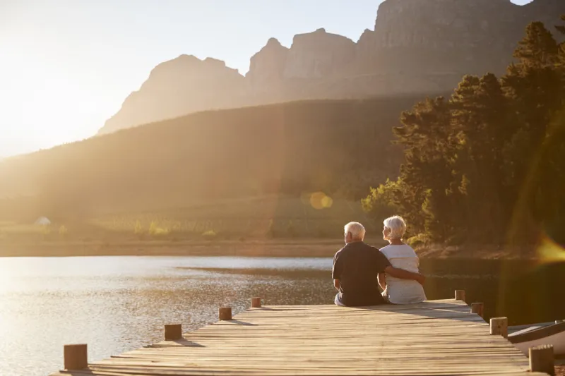 romantic senior couple sitting on wooden jetty by lake