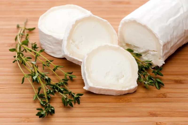 slices of goat cheese with fresh thyme on a bamboo cutting board