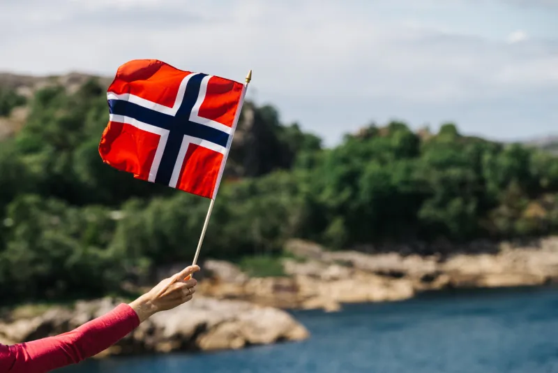 tourist hand holding norwegian flag on rocky stone sea coast background