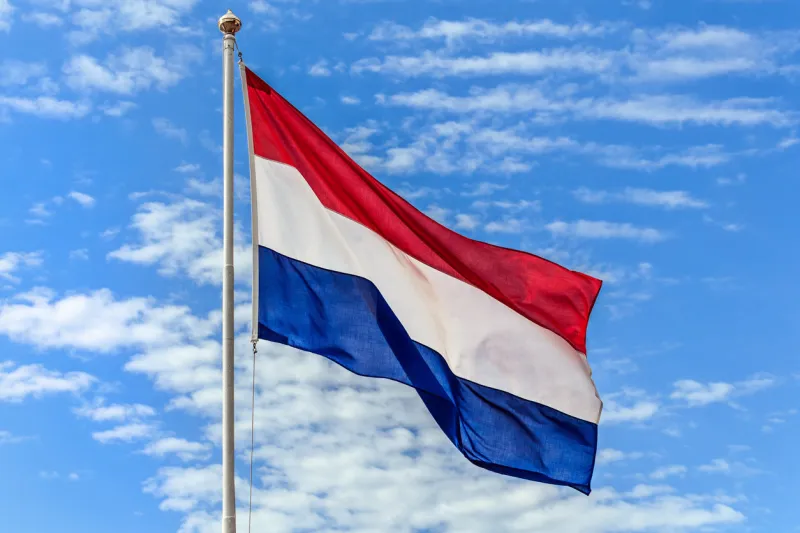 the national flags of the netherland flag on the background of blue sky with clouds