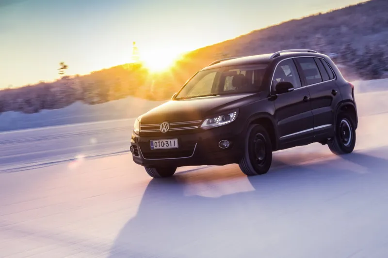 nokia, finland - february 2, 2018  black suv volkswagen tiguan drives on a flat snow surface in lapland bright sunlight glare seen over a hill in a background color toning applied in post-production