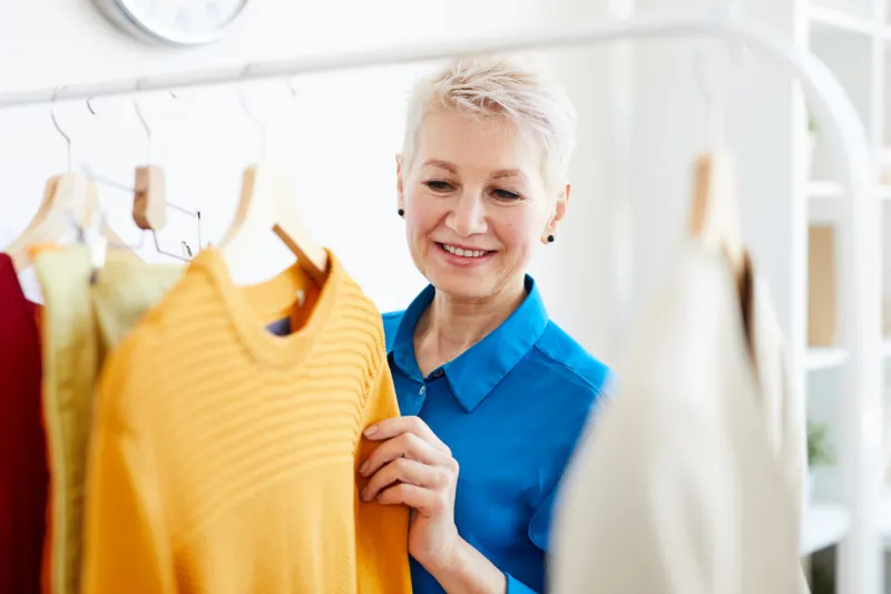 happy blonde female choosing proper pullover from new collection of casual clothes while visiting boutique