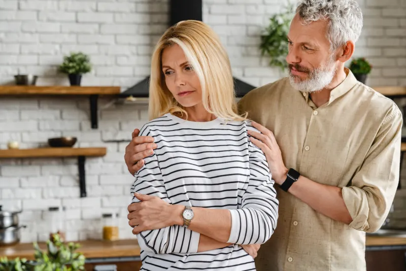 handsome mature man calming his upset wife while both standing at home