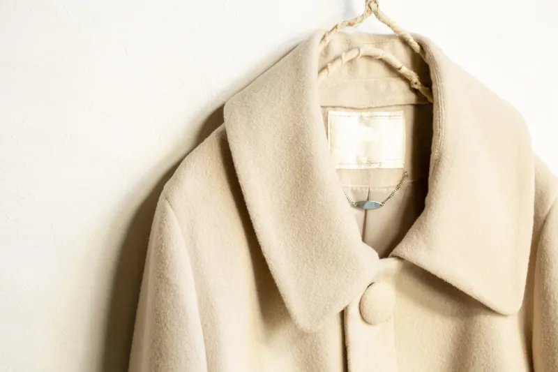 beige wool coat hanging on clothes hanger on white backgroundclose up