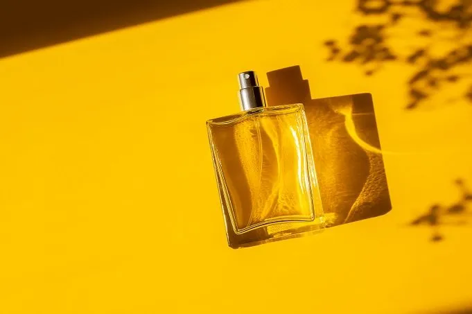 transparent bottle of perfume on a yellow background fragrance presentation with daylight trending concept in natural materials with beautiful shadow women's essence