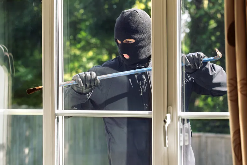 burglar breaking into a house via a window with a crowbar