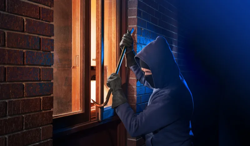 burglar using crowbar to break into a house at night with room left and right for type