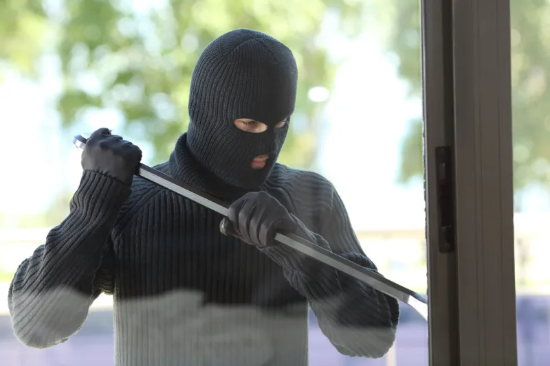 thief wearing black mask trying to open a house window with a lever