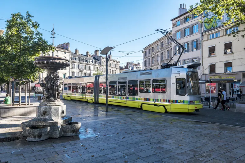 saint-etienne, france - july 29, 2019 street view in saint etienne downtown the tramway passing along the square place du peuple the statue with fountain is at foreground