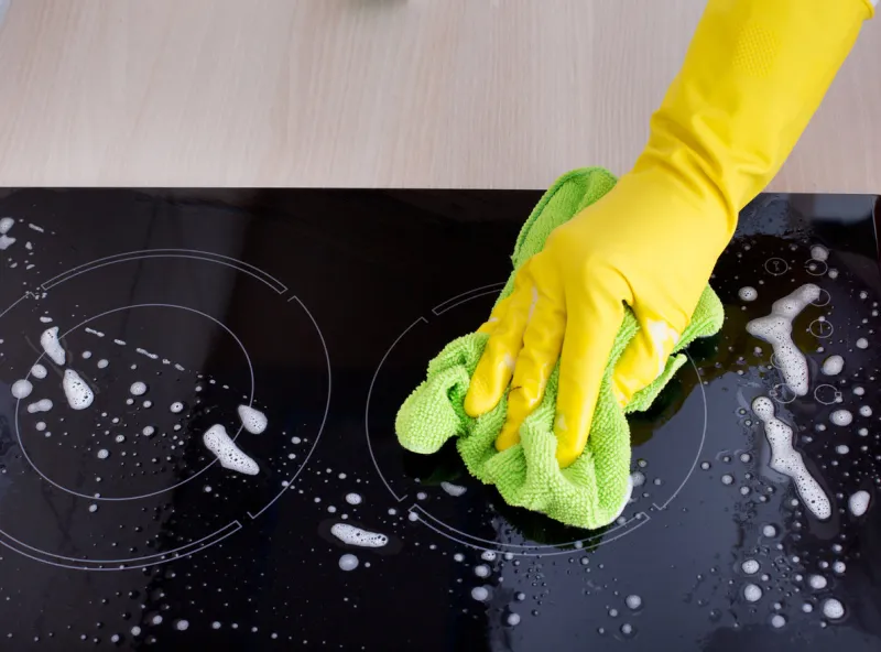 close up of human hand with protective gloves cleaning induction hob with green mop
